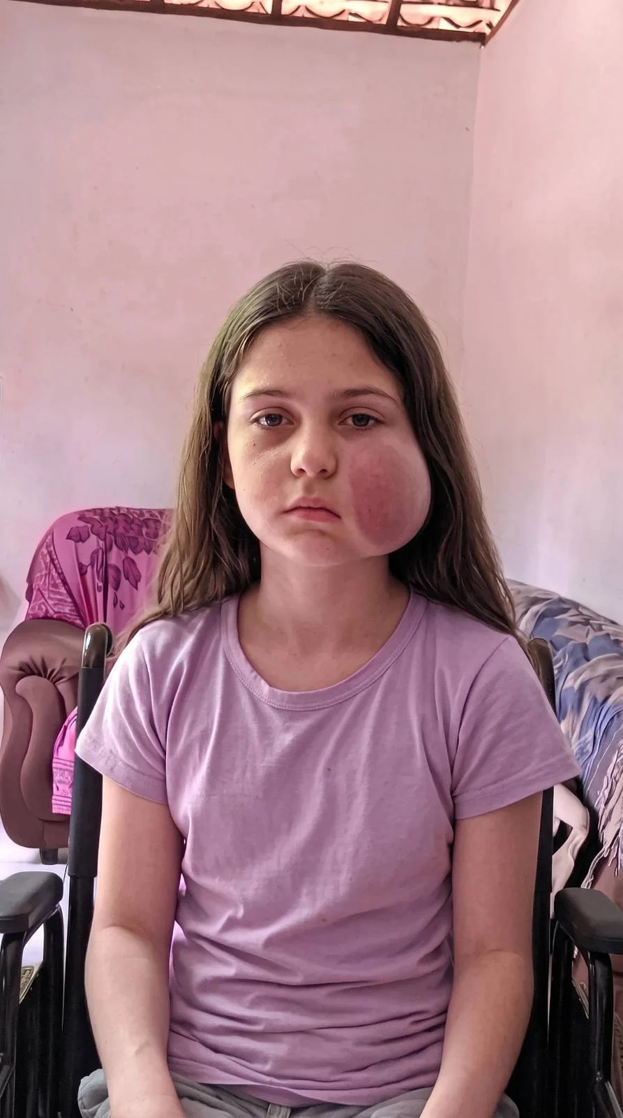 Larissa sentada em sua cadeira, usando uma camiseta lilás.